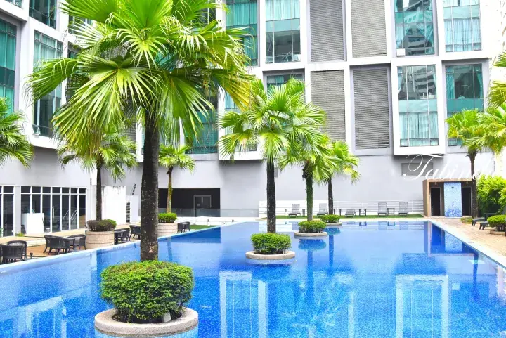 Modern hotel pool with palm trees and lounge chairs surrounded by glass-fronted accommodation buildings.