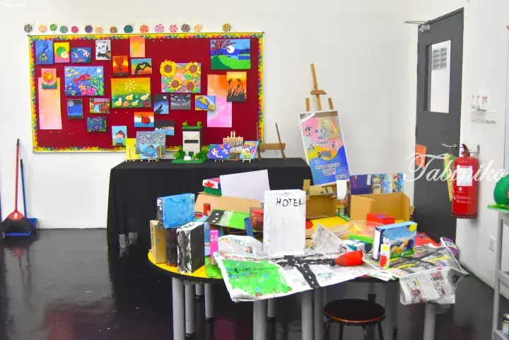 Colorful children’s artwork displayed on a red bulletin board and cardboard sculptures on a table in an art classroom.