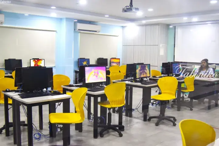 Modern computer lab with yellow chairs, white desks, and monitors in a bright room with air conditioning.