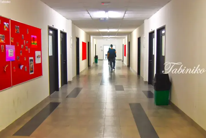 Long hallway with red bulletin boards and doors, showing a person walking away in a modern building.