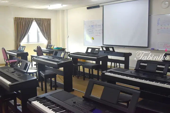 Music classroom with multiple digital pianos, whiteboards, and a projector screen for lessons.