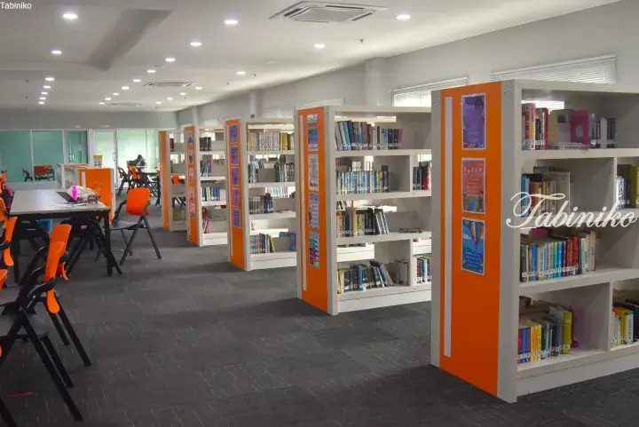 Bright library interior with white bookshelves, orange accents, and study tables in a modern Malaysian facility.