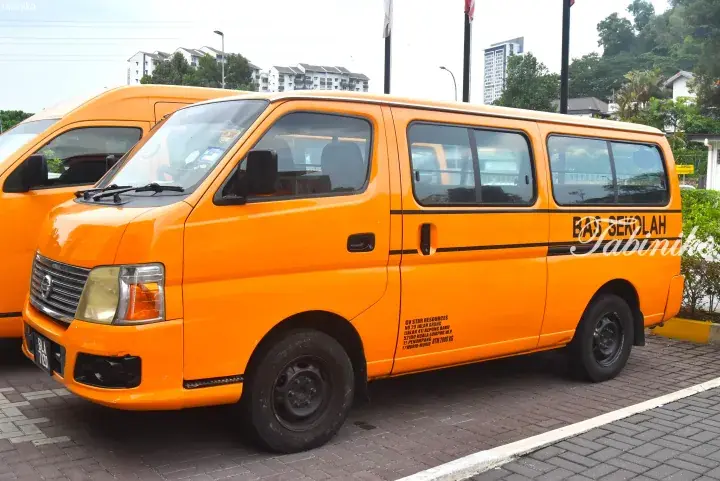 Bright orange Nissan Urvan school bus parked in a lot, displaying ‘BAS SEKOLAH’ text and GV Star Resources details.
