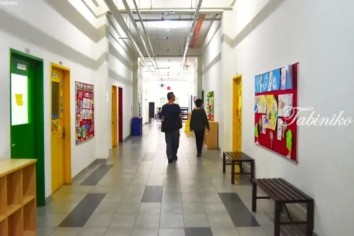 A hallway in a Malaysian preschool with colorful doors and children’s artwork displayed on the walls.