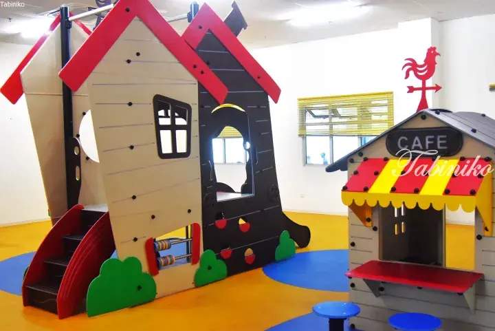 Colorful indoor playground with a house-shaped climbing structure and a cafe playhouse for children.