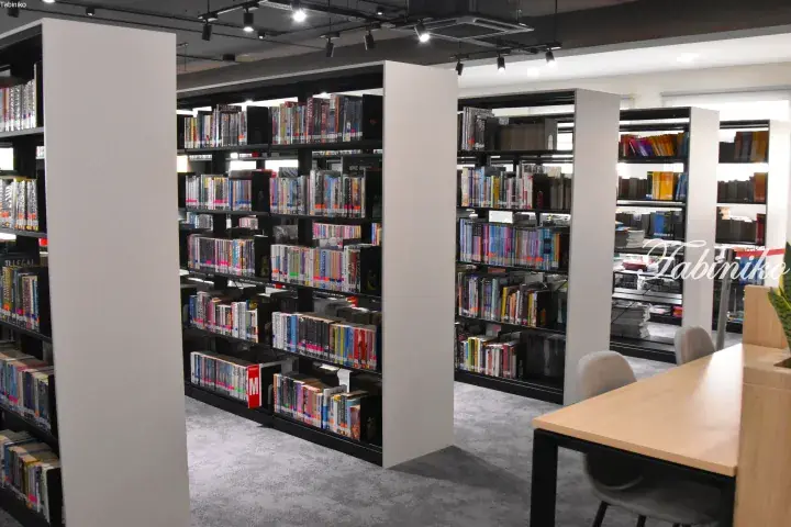 Modern library interior with black bookshelves, white pillars, and a wooden reading table.