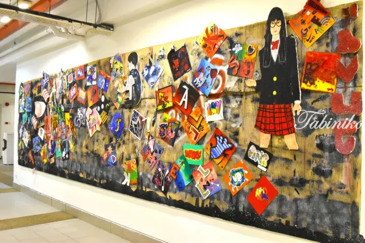 Colorful student artwork and a schoolgirl figure displayed on a textured wall in a school corridor.