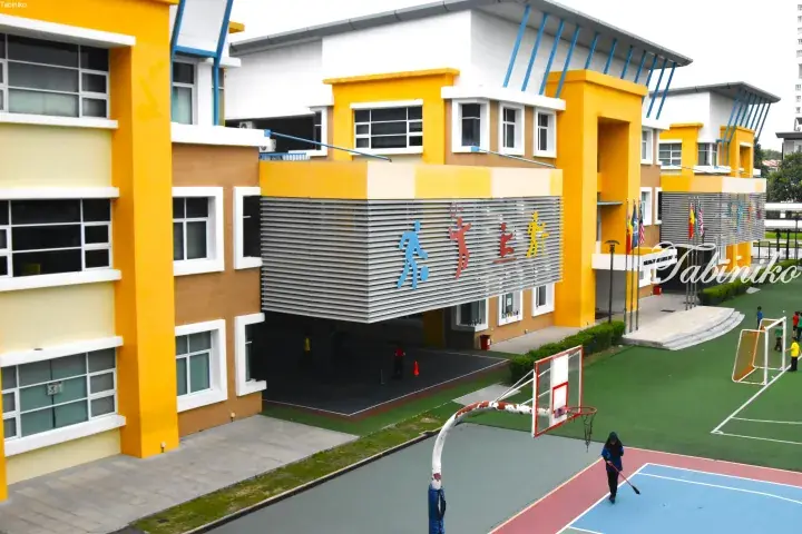 Modern school building with yellow and white facade, sports court, and colorful athletic figures on the exterior.