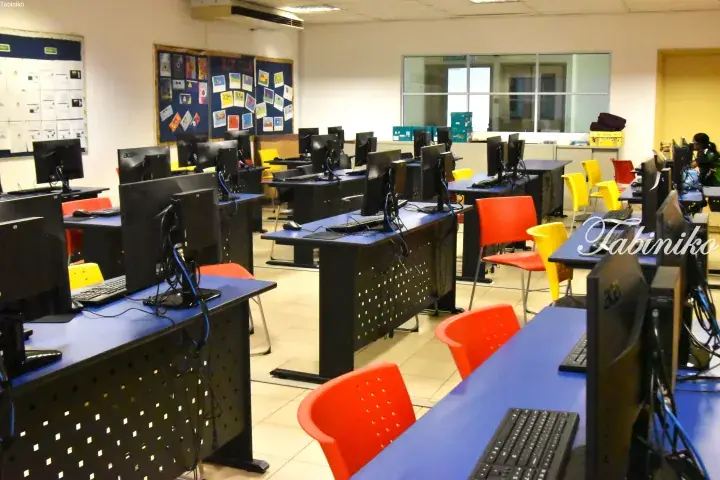Rows of desktop computers with blue desks and colorful chairs in a modern computer lab.