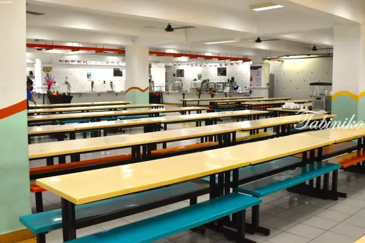 Spacious school cafeteria with rows of yellow tables and colorful benches in a bright, clean dining area.