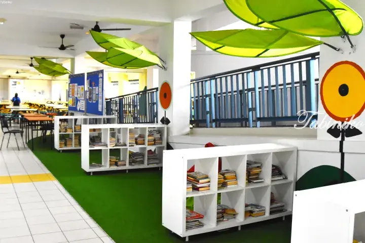 Colorful children’s reading area with white bookshelves, green artificial grass, and large leaf decorations in a Malaysian school.