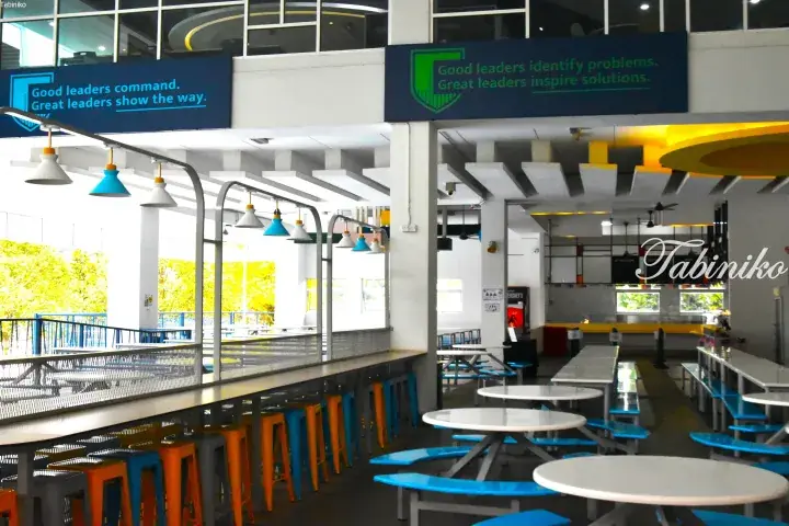 Modern university cafeteria with blue and orange stools, motivational leadership quotes on wall banners.