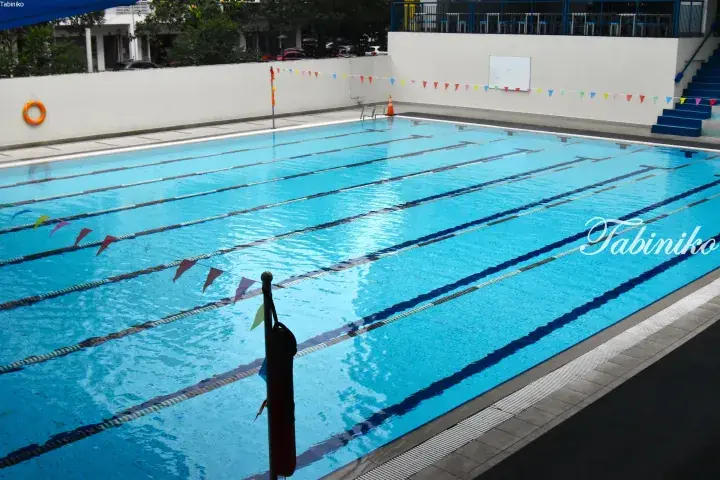Outdoor swimming pool with lane ropes and colorful flags at a residential complex in Malaysia.