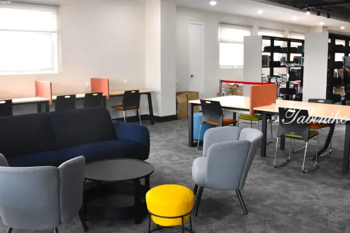 Modern co-working space with blue sofa, grey chairs, yellow stool, and study desks with orange partitions.
