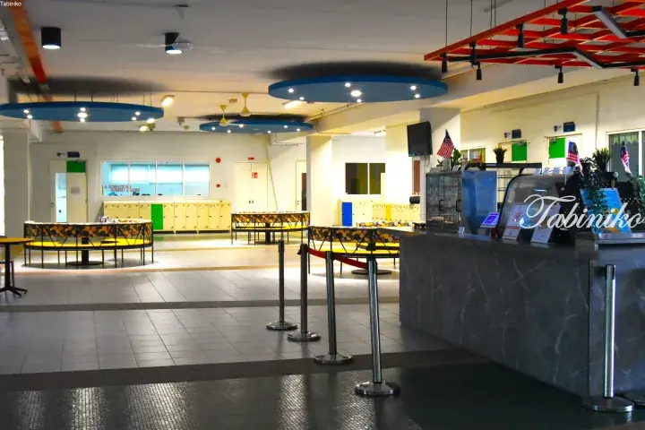 Modern interior of a Malaysian food court featuring circular seating, blue ceiling accents, and a service counter with Malaysian flags.