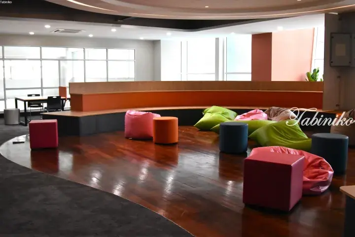 Modern co-working space with colorful bean bags and circular wooden seating area near large windows