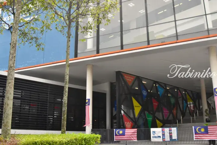 Modern KDU College building entrance with Malaysian flags and colorful welcome banners.