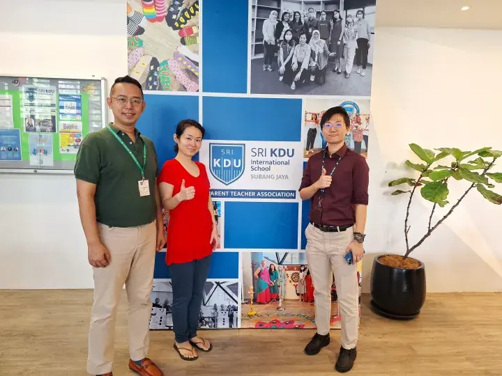 Three people pose with thumbs up in front of a Sri KDU International School Subang Jaya Parent Teacher Association banner.