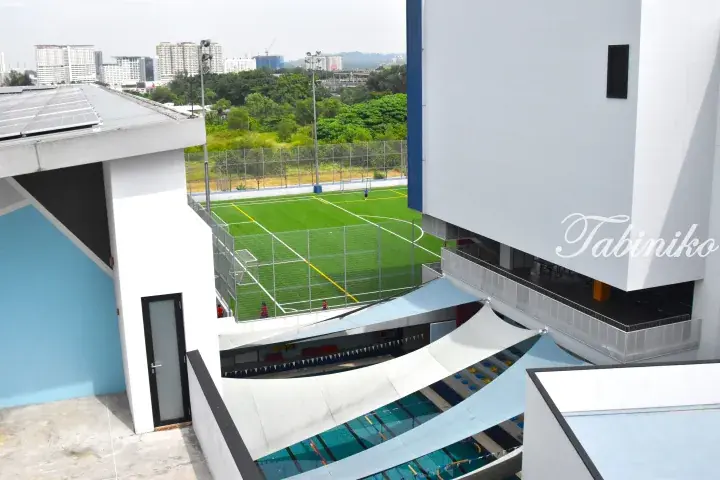 View of a modern sports complex featuring an artificial turf football pitch and an outdoor swimming pool with shade sails.