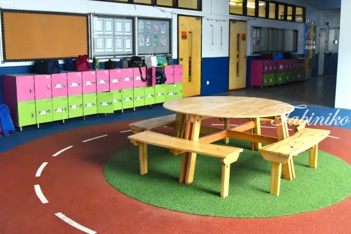 Colorful lockers and wooden picnic table in a bright school hallway with red and green flooring.