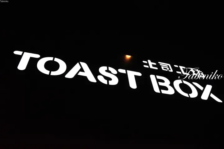 Illuminated TOAST BOY sign with Japanese text on a dark background, representing a popular Malaysian cafe.