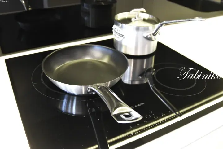 Modern Bosch induction cooktop with a stainless steel frying pan and saucepan on a sleek black surface.