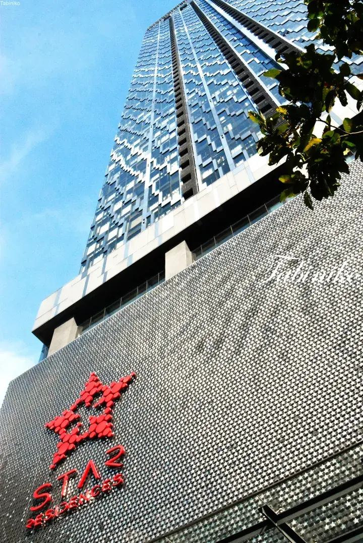 Modern glass skyscraper with distinctive facade above a textured wall featuring the red STAR Residences logo.