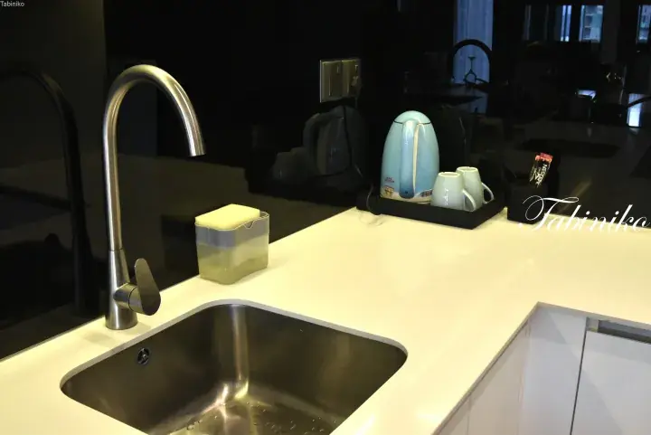 Modern kitchen sink with stainless steel faucet and white countertop, featuring a kettle and coffee supplies in a Malaysian apartment.