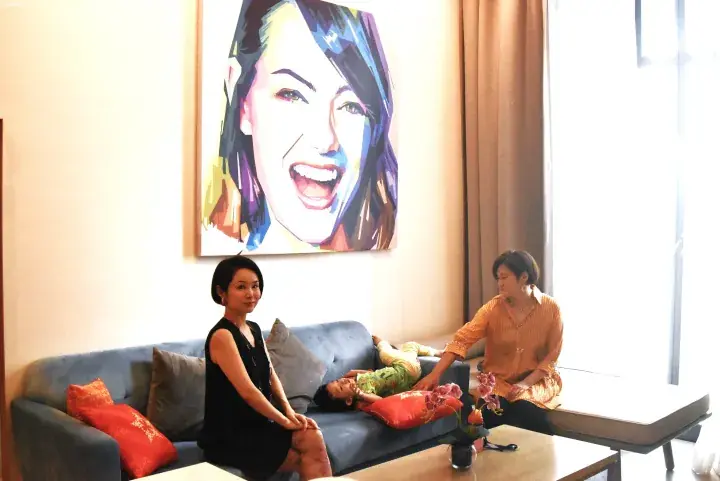 Two women and a child relaxing on a sofa in a modern living room with a large colorful portrait on the wall.