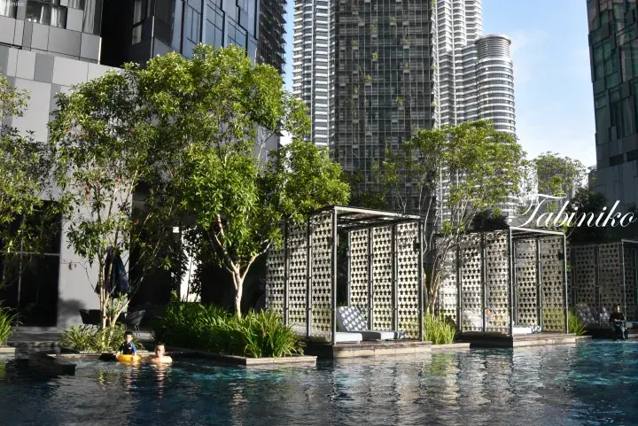 Swimming pool with cabanas and trees at a KLCC residence, with Petronas Towers visible in the background.