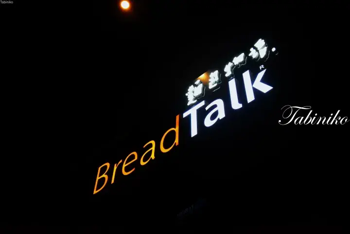 Illuminated BreadTalk sign with Japanese characters against a dark night sky.