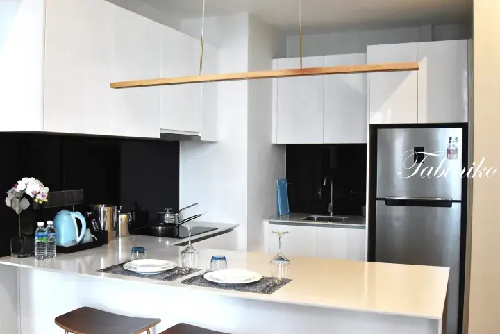 Modern kitchen with white cabinetry, black backsplash, and a breakfast bar set for two in a Malaysian apartment.
