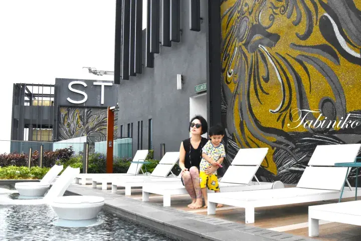 Woman and child relaxing by a rooftop pool with white loungers and a large golden tiger mural at a modern property.