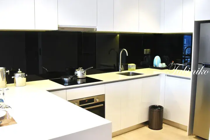 Modern white kitchen with black glass backsplash, induction cooktop, and stainless steel appliances in a serviced residence.