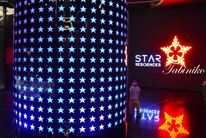 A child stands near a glowing blue star-patterned pillar and a large red star sign at Star Residences.
