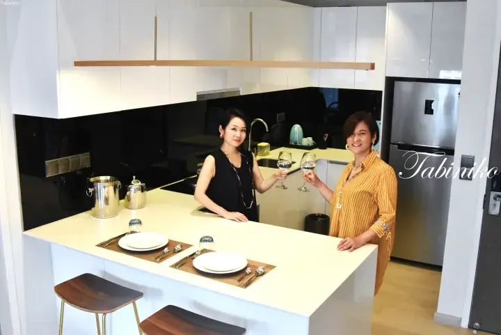Two women toast with wine glasses in a modern white kitchen featuring an island counter and sleek cabinetry.