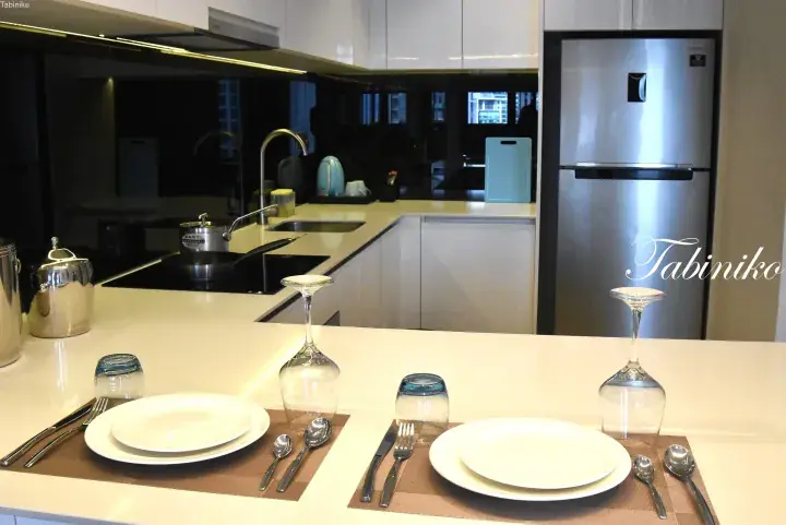 Modern kitchen with white countertops, stainless steel appliances, and a dining area set for two with wine glasses.