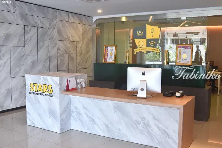 Reception desk at Stars International School with marble finish, computer, and awards display behind glass partition.