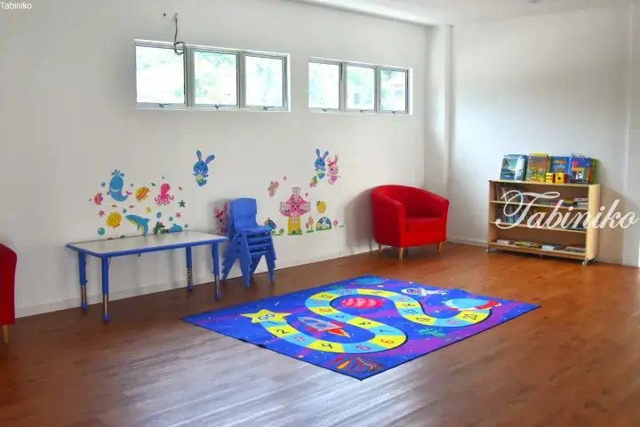 Bright children’s playroom with wooden floors, colorful wall decals, a space-themed rug, and child-sized furniture.