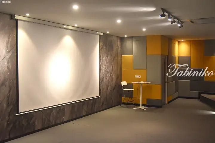 Modern meeting room with large projector screen, marble walls, and yellow acoustic panels.