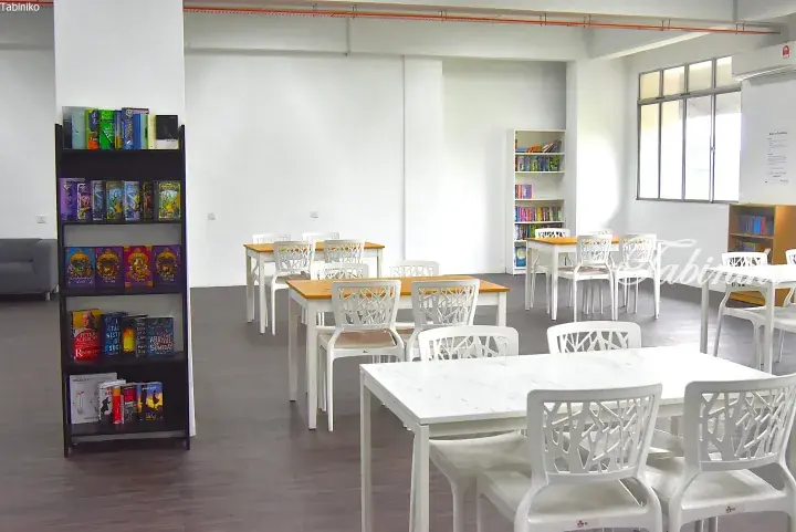 Bright study area with white tables and chairs, bookshelves, and large windows in a modern co-working space.