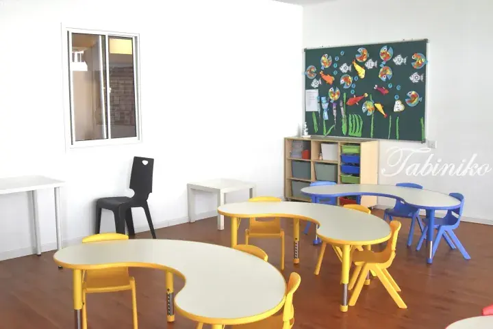 Bright classroom with colorful curved tables and chairs, a bulletin board with fish decorations, and wooden flooring.