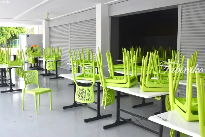 Stacked lime green chairs on white tables in a clean, modern cafeteria with roller shutters.