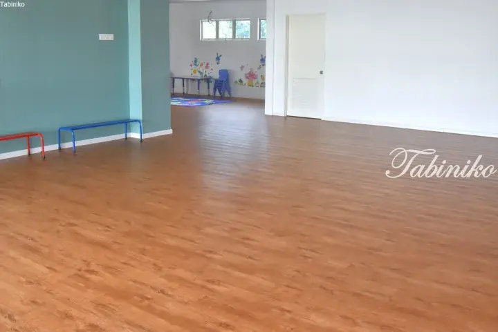 Spacious room with wooden flooring, blue and red benches, and a children’s play area in the background.