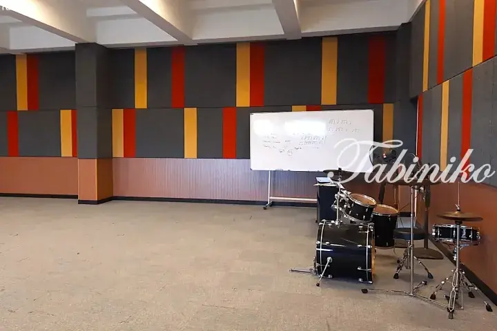 Spacious music practice room with colorful acoustic wall panels, a whiteboard, and a drum set ready for use.
