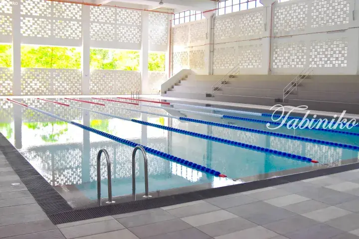 Indoor swimming pool with lane ropes and tiered seating, featuring decorative perforated walls and natural light.