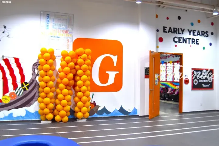 Bright entrance to a Malaysia early years centre featuring orange balloon columns and a large G logo on a white wall.