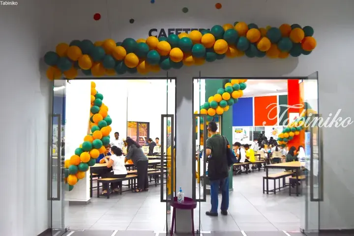 Cafeteria entrance decorated with yellow and teal balloons, with students dining inside.