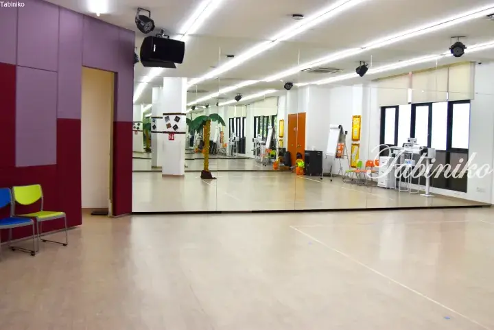Bright dance studio with floor-to-ceiling mirrors, wooden flooring, and colorful chairs.