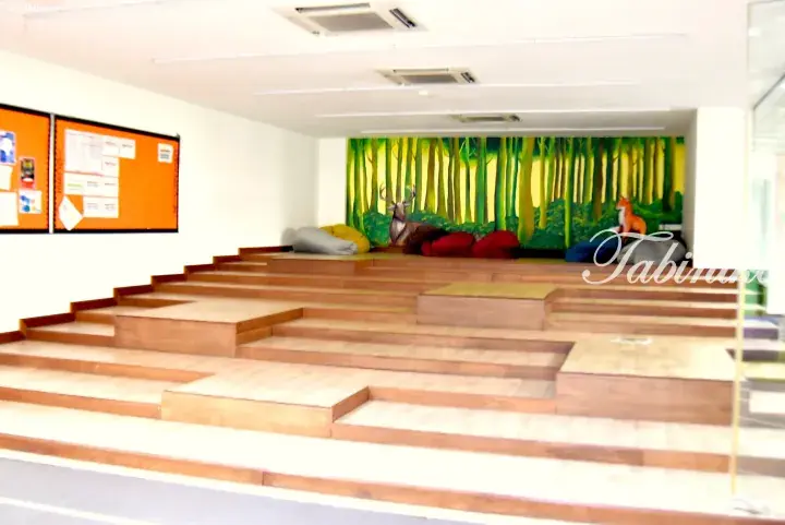 Wooden tiered seating area with bean bags and a forest mural in a modern Malaysian space.